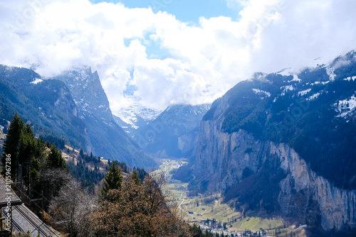 A breathtaking, vertical landscape photograph showcasing the dramatic u-shaped Lauterbrunnen Valley nestled deep between massive limestone cliffs in the Bernese Oberland region. Captured from an eleva