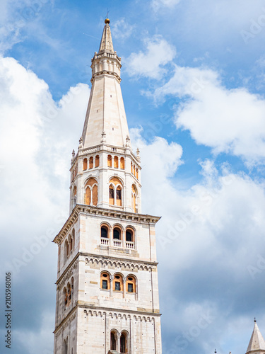 Ghirlandina Tower rising against a bright cloudy sky, showcasing the Romanesque architecture of the UNESCO World Heritage Site in Italy