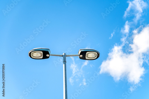 Twin streetlight beneath blue sky with white clouds in a clean modern urban setting