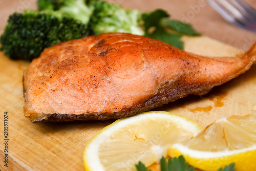 flat lay of grilled salmon on a wooden cutting board, garnished with fresh vegetables on the side	