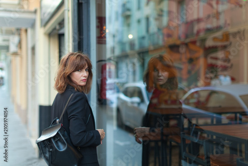 Cuadro en lienzo Woman with brown hair wearing a black coat and backpack glancing at a glass stor