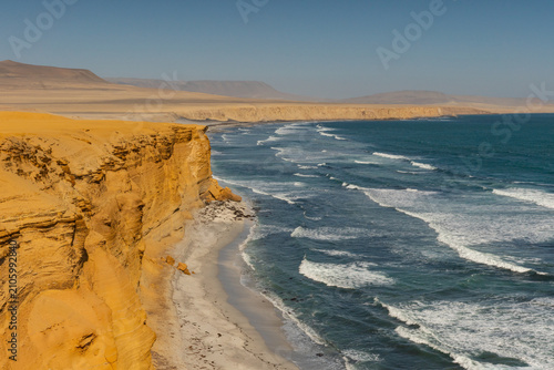 Golden sandstone cliffs overlooking breaking Pacific Ocean waves along the rugged desert coastline of Paracas National Reserve, Peru