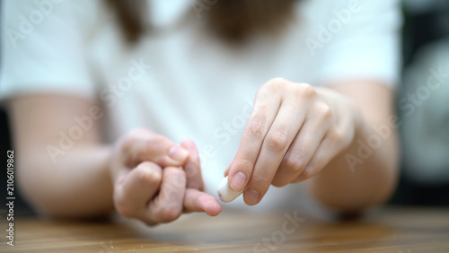 Fotografía Woman carefully pricks her finger with a white lancet to collect a blood sample for medical analysis and health testing