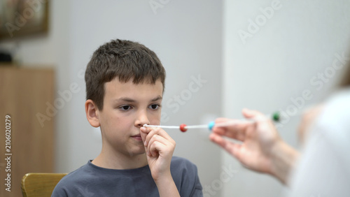 Mother helps her young son practice a vision therapy exercise with a colorful beaded string to improve eye coordination and focus at home.
