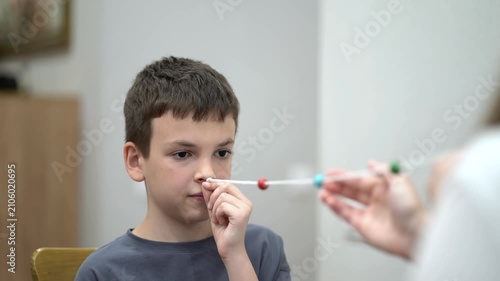 Mother helps her young son practice a vision therapy exercise with a colorful beaded string to improve eye coordination and focus at home.