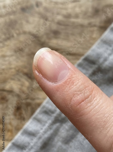 Macro Close-Up of a Bare Thumb Showing Natural Nail Plate, Cuticle and Detailed Skin Texture, Against a Blurred Wooden Background
