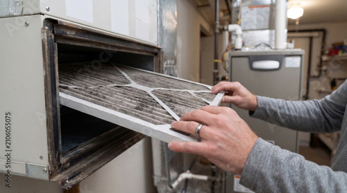 Closeup of a mans hands removing a dirty, dustcovered hvac air filter from a residential furnace unit for replacement or maintenance