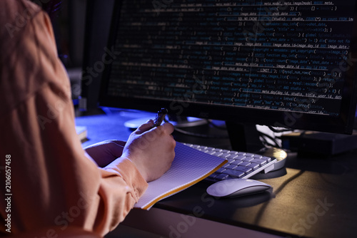 Female programmer working with notebook and computer in dark office at night,...