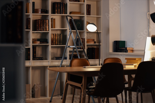 Tableau sur toile Interior of library with table, stepladder and bookshelf in evening