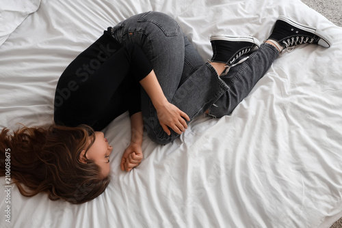 Sad young woman lying on bed, top view