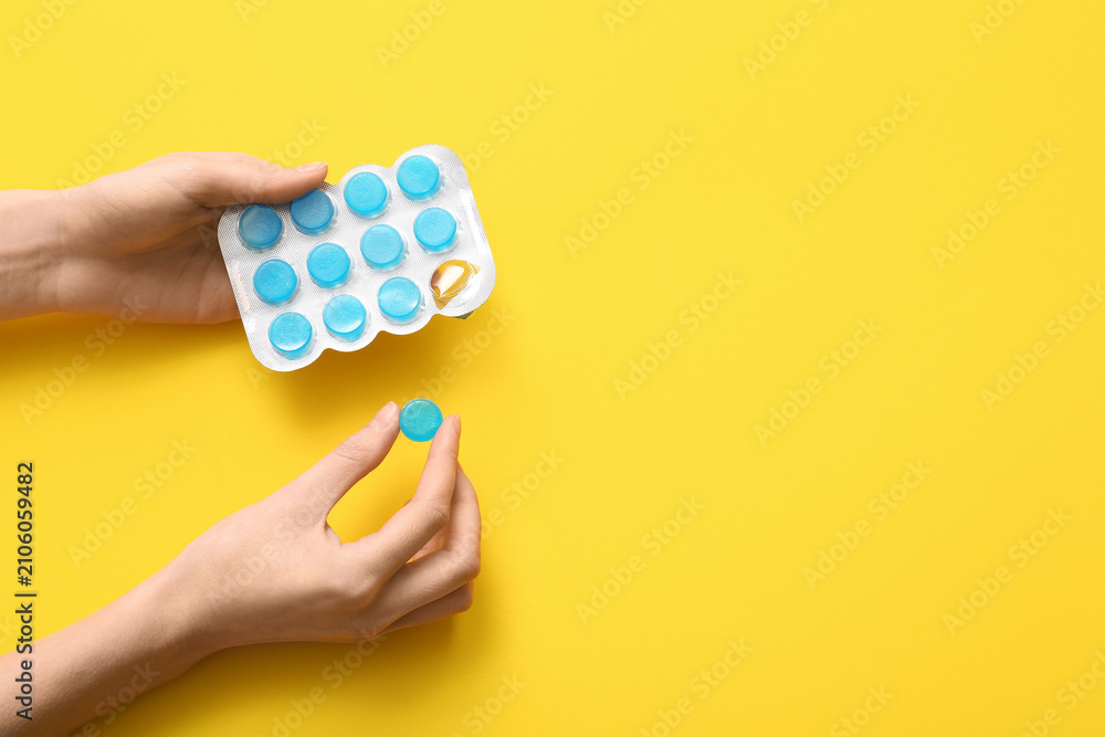 Obraz premium Female hands with cough drops in blister on yellow background