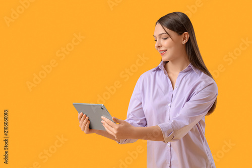 Beautiful young woman with modern tablet computer on yellow background