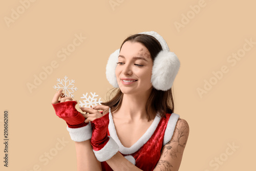 Beautiful young woman dressed as Santa Claus with decorative snowflakes on be...