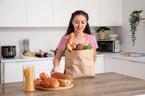 Beautiful young Asian woman with bread and paper bag full of fresh products i...