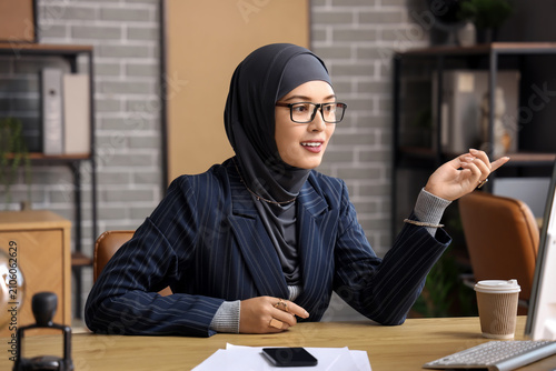 Muslim businesswoman video chatting at table in office