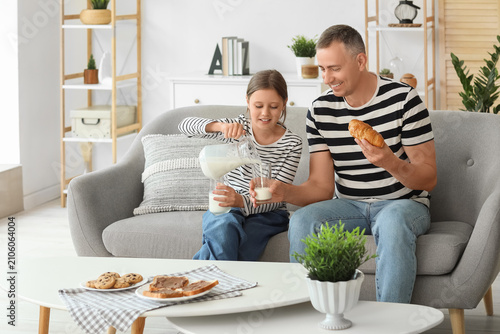 Photography Little girl with her father sitting on sofa, drinking milk and eating pastries i