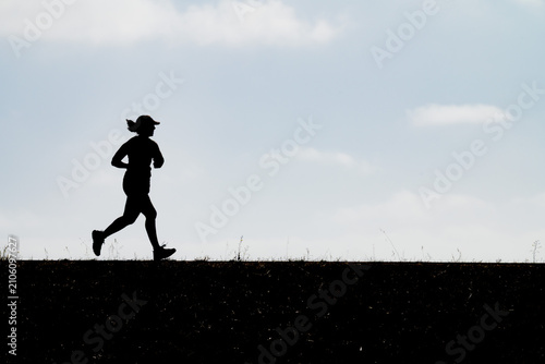 Bild auf Leinwand Dynamic full-body silhouette of a female runner jogging along a crest symbolizing athletic training outdoor marathon practice healthy living endurance and energetic motion under an expansive sky