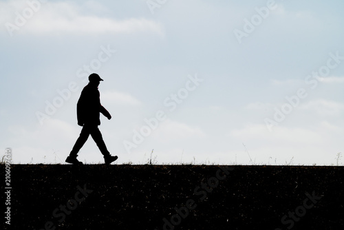 Φωτογραφία Minimalist profile silhouette of a man wearing a cap walking purposefully along a ridge under a bright sky representing casual exercise outdoor recreation daily stride and active healthy living