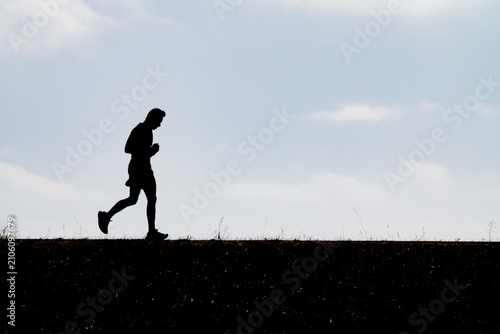 Foto Dynamic silhouette of a male runner mid-stride against a expansive light sky symbolizing athletic determination cardio fitness training discipline and vigorous outdoor exercise