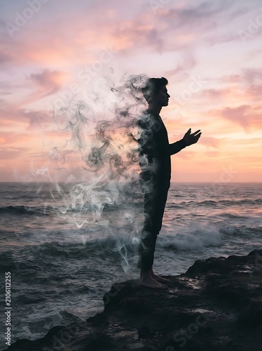 A man standing on a rocky cliff dissolving into smoke against a sunset ocean background.