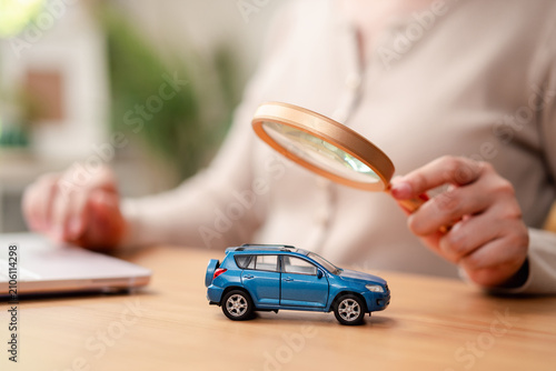 Online car search and car hunting concept. Blurred woman hand holding magnifying glass over a blue toy car near laptop.