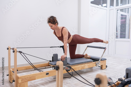 Pilates reformer exercise performed by woman in brown athletic wear inside a bright minimalist fitness studio
