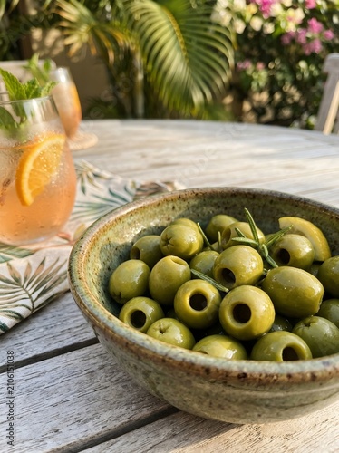 Bowl of Green Olives with Rosemary on Outdoor Table Beside Citrus Cocktail