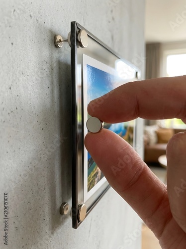 Close-Up of Fingers Attaching a Metal Standoff to a Frameless Acrylic Photo Print Mounted on a Textured Concrete Wall Using Nickel Wall Mounts