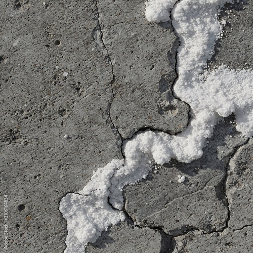 White salt deposits filling deep cracks in a rough grey concrete surface