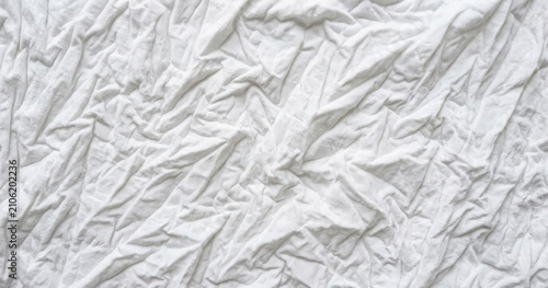 View of white fabric with deep folds and creases, soft shadows creating a textured surface pattern for backgrounds