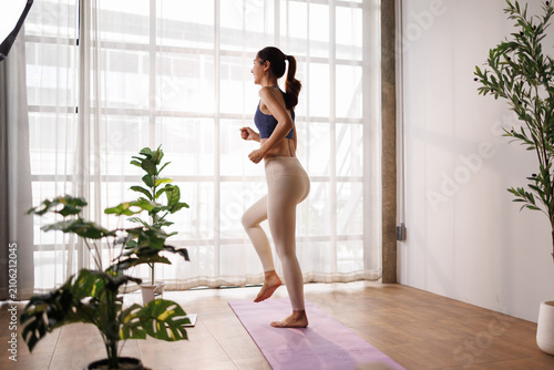 Billede på lærred Young energetic asian woman exercising at home, raising knee during an active wo