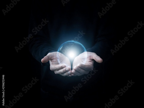 Human hands cupped together holding a glowing blue sphere of light against black background