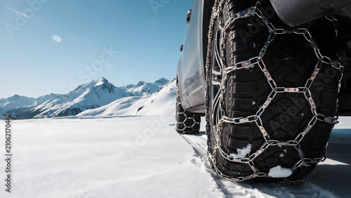 Vehicle tire with metal snow chains driving on a snowy mountain road