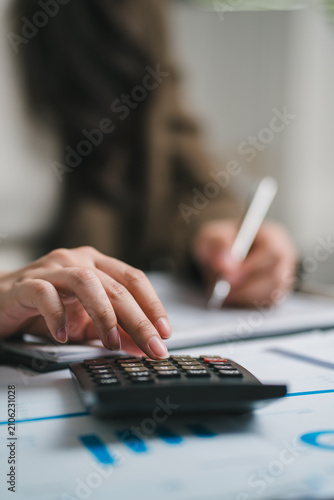 Close-up of a businesswoman hand using a calculator to review financial charts, budgeting business plan and taking notes on a document at her office desk