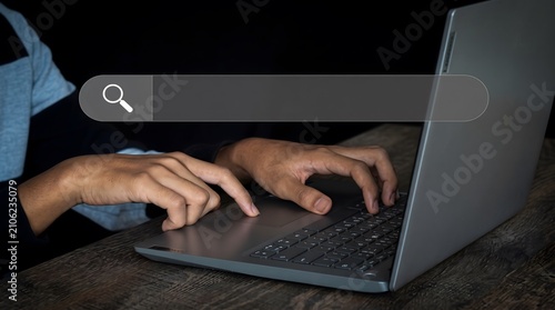 Person typing on laptop computer with floating digital search bar interface in darkened room setting