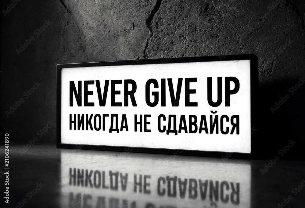 Naklejka premium Motivational sign with never give up message in english and another language on table surface