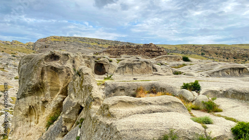 Rock-cut caves spread across Uplistsikhe in a wide ground-level view, revealing carved chambers, eroded sandstone surfaces