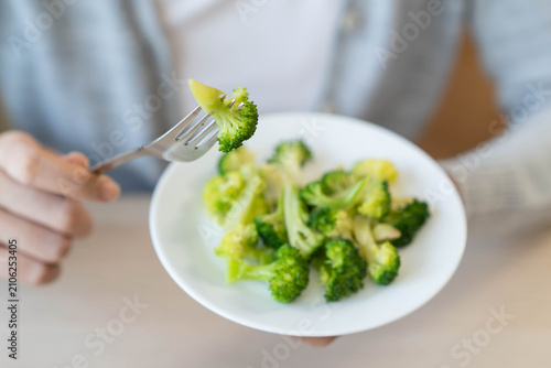 Foto Close up of a woman hand holding fork with green broccoli over a white plate for