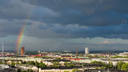 A vibrant rainbow arches over the urban skyline under dark storm clouds
