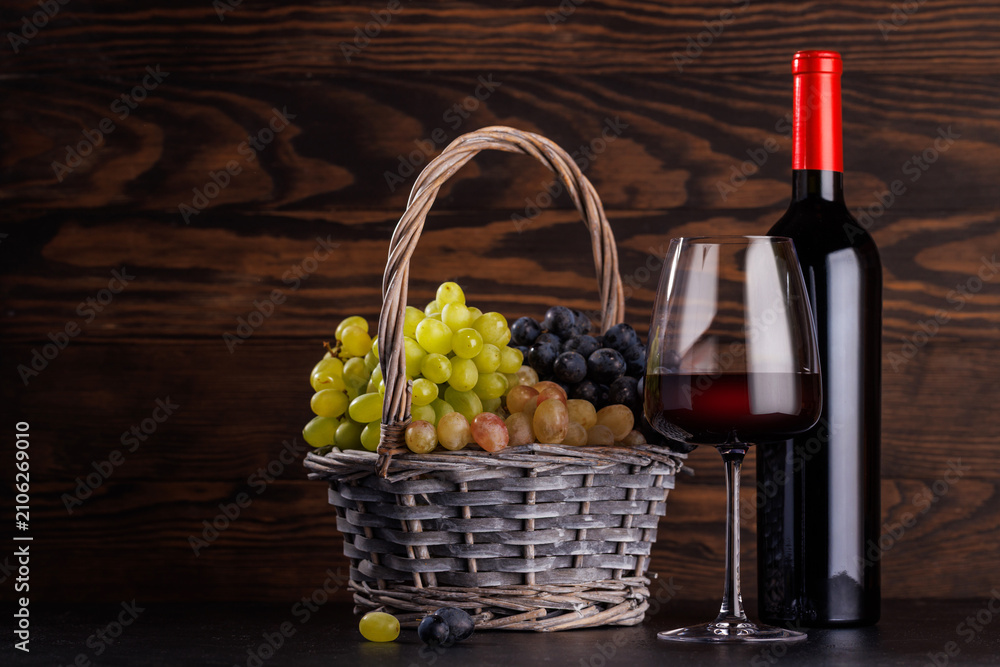 Obraz premium Red wine bottle with a glass and basket of fresh grapes