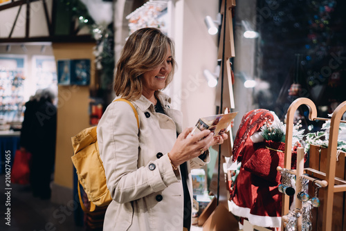 Fotografija Caucasian woman traveler holding greeting card in festive gift shop, happy lady