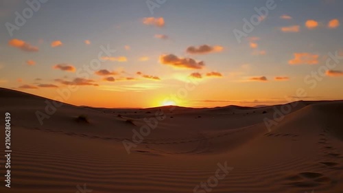 Golden sun sets over the vast rolling sand dunes of the desert
