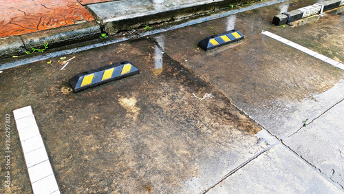 Parking Curb Reflections: Black and Yellow Striped Wheel Stopper in Empty Parking Space After Rain.