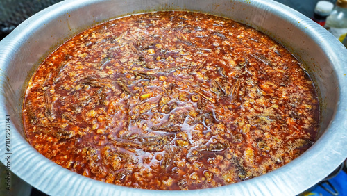 Rich Stew in Pot: Traditional Thai Red Curry Sauce with Minced Pork and Chili Oil in Big Cooking Pot. A close-up shot showcases a hearty and flavorful stew simmering in a large metal pot, its rich red