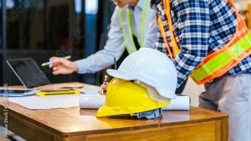 Construction team meeting with hard hats, laptop and blueprints on a desk, showing planning, safety and teamwork at a worksite