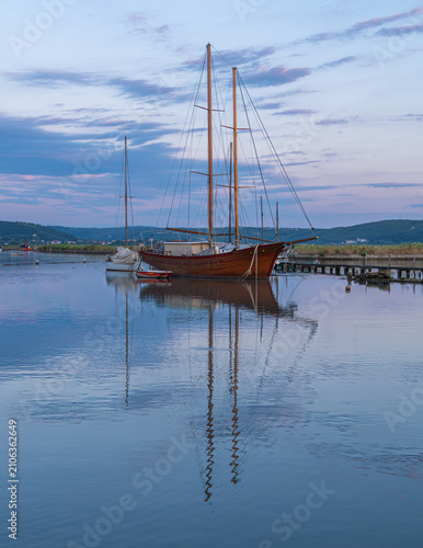 Wooden sailboat reflected in calm harbor at dusk