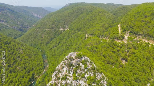 Cakallar, Alanya, Turkey. Alara Castle, stone fortress ruins crowning a white limestone crag above the Alara River gorge, sweeping aerial drone view over dense pine forests and the Taurus Mountains. 