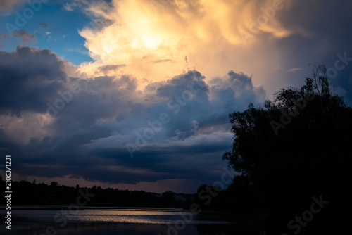 Canvastavla Rolling clouds part to reveal a brilliant sunlit core above a mirrorlike lake as