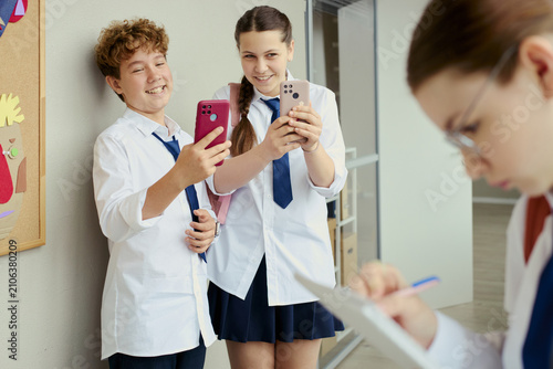Canvastavla Teenage boy and teenage girl using smartphones in school hallway, smiling and sharing social media content while classmate studying nearby