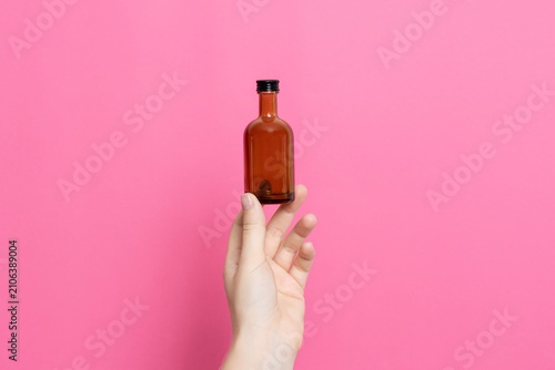 Hand holding small brown glass bottle on pink backdrop